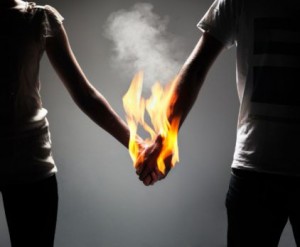 bad love, trauma bonding, couple hands joined on fire black and white image with orange fire