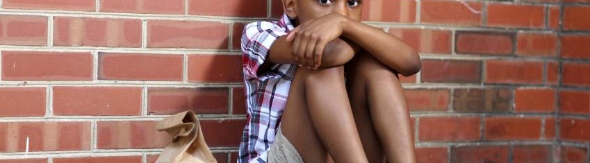 homeless schoolboy sitting on ground against wall
