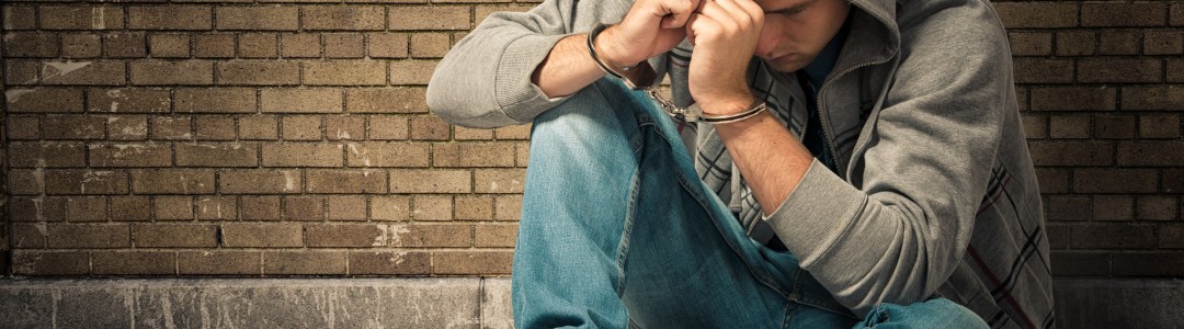 handcuffed young man sitting on ground in corner